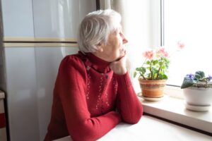 Older woman looking out of a window at home, illustrating behavioural and emotional changes in later life.